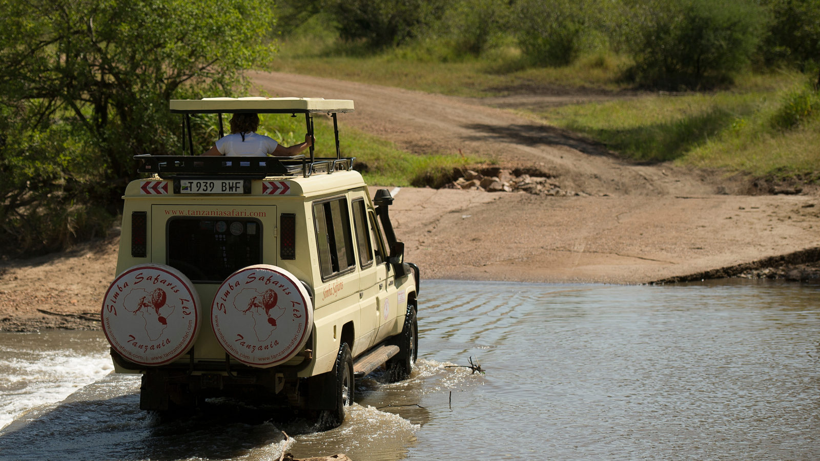 a Toyota Land Cruiser vehicle with raised top crossing a shallow river