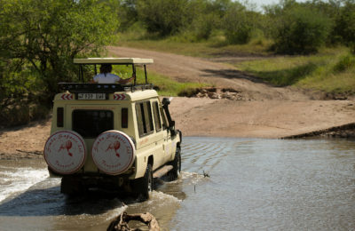 a Toyota Land Cruiser vehicle with raised top crossing a shallow river