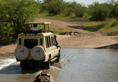 a Toyota Land Cruiser vehicle with raised top crossing a shallow river